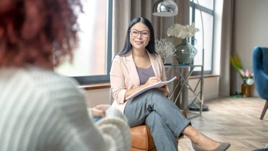 Pleasant psychologist. Pleasant psychologist wearing grey trousers smiling to client while speaking with her